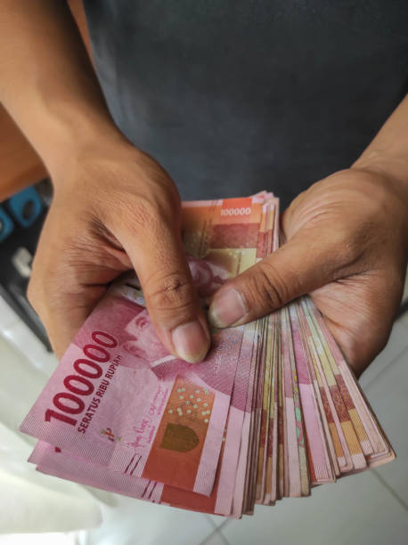 Asian man holding Indonesian Rupiah Money bills for giving, bribing, paying, counting concept.